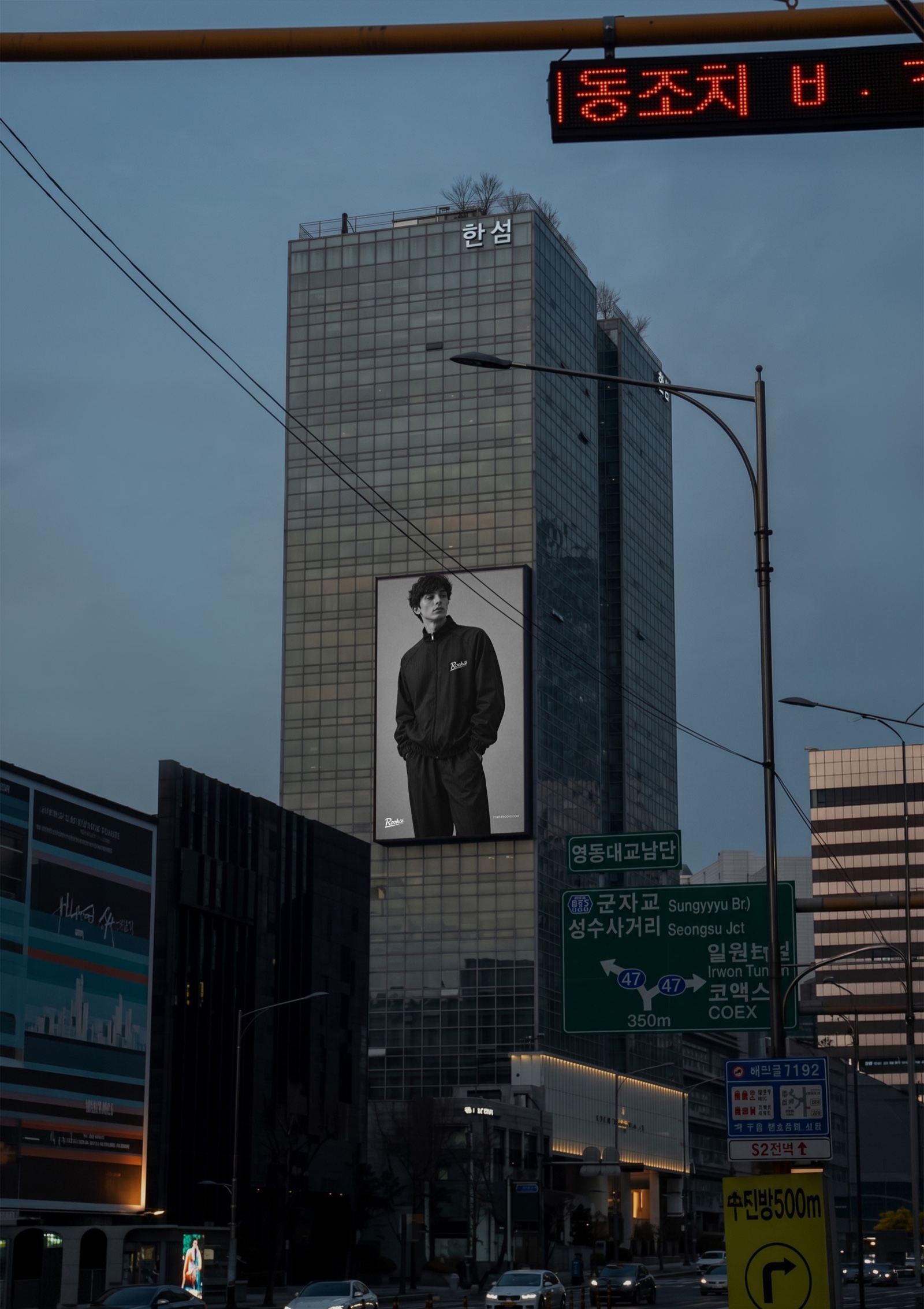 Rookie tracksuit campaign on a tower screen in Seoul at dusk