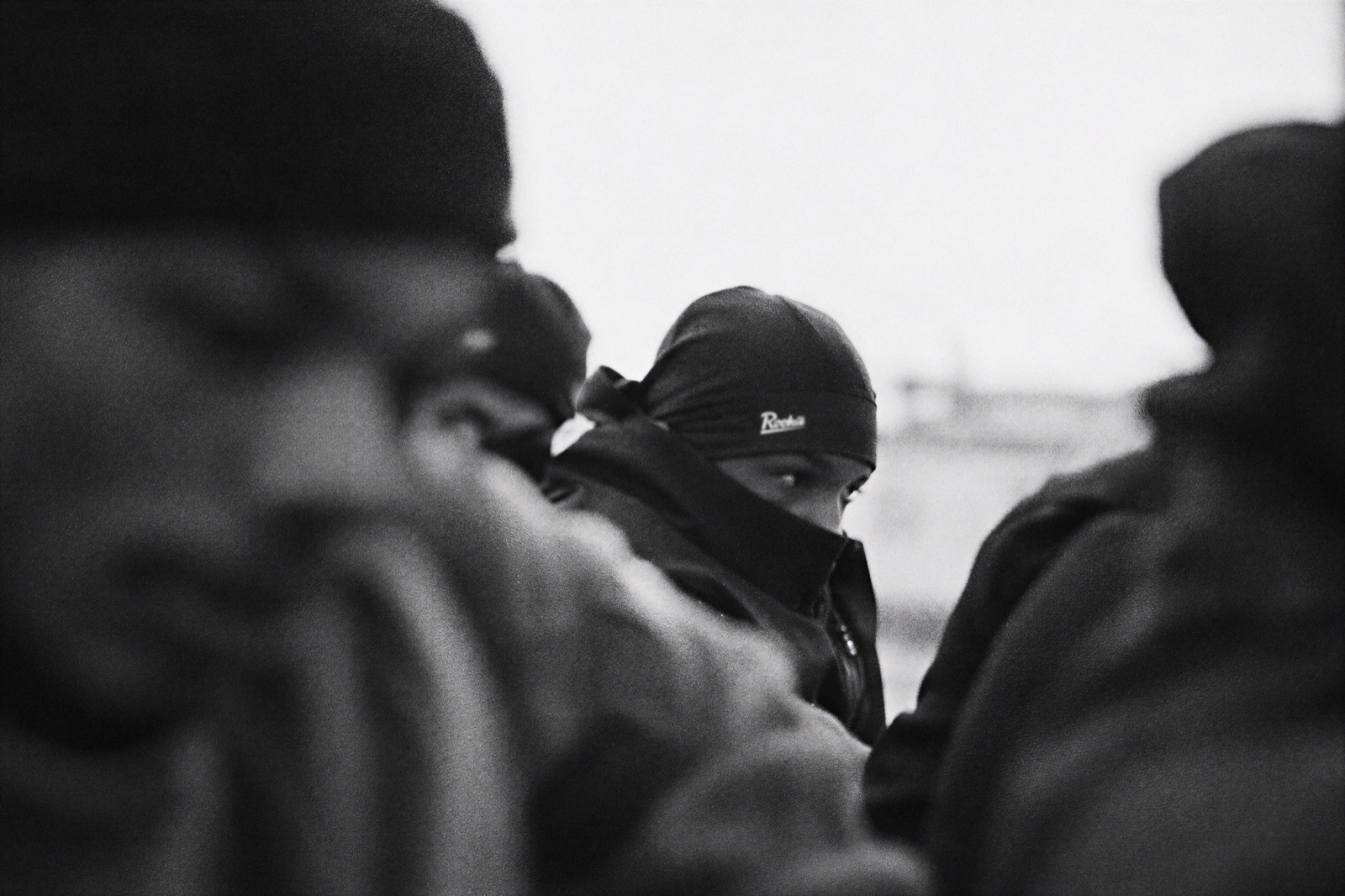 Black-and-white crowd with one face in a Rookie durag looking through