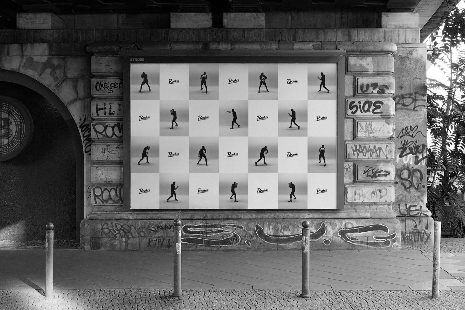 A checkerboard of boxer photographs and Rookie logos in a street poster frame under a graffitied bridge